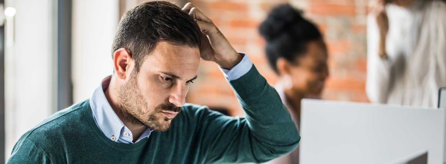 Man withhand on head at a computer